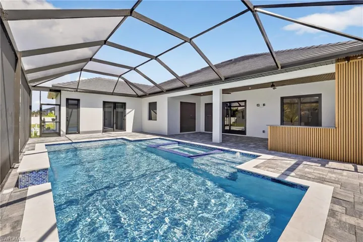 View of pool with a patio area, a pool with connected hot tub, and glass enclosure