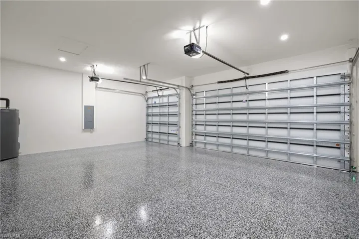 Garage featuring electric panel, water heater, a garage door opener, and recessed lighting
