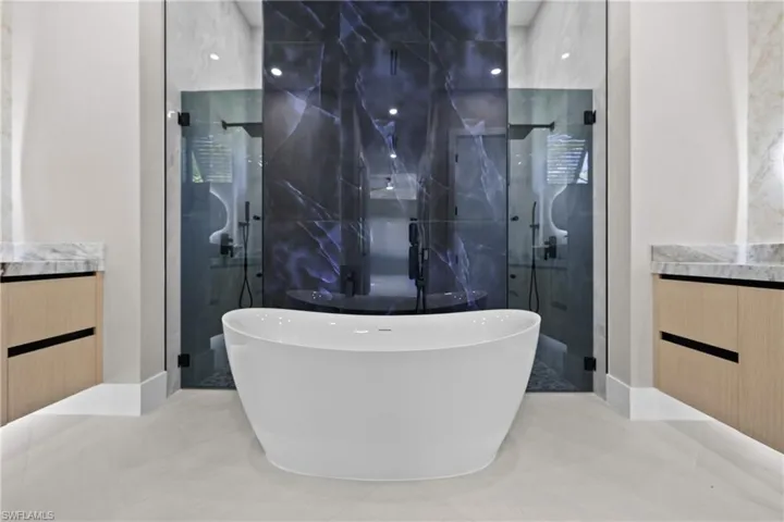 Bathroom with vanity, a stall shower, a freestanding tub, tile patterned floors, and tile walls