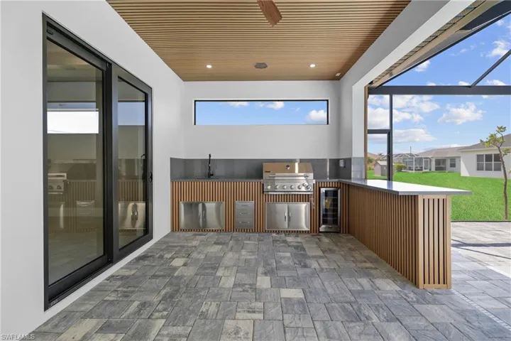 View of patio with exterior kitchen, beverage cooler, a ceiling fan, and a lanai