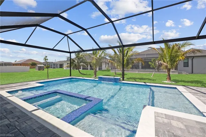 View of swimming pool featuring a lawn, a pool with connected hot tub, glass enclosure, and a patio area