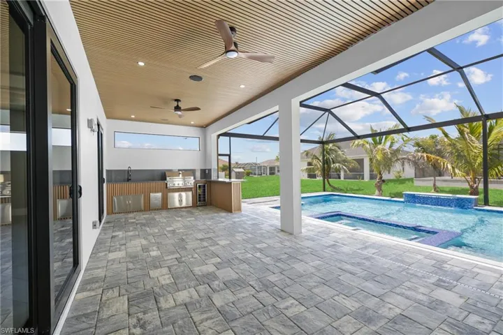 View of pool featuring an outdoor kitchen, a ceiling fan, a lawn, a patio, and glass enclosure