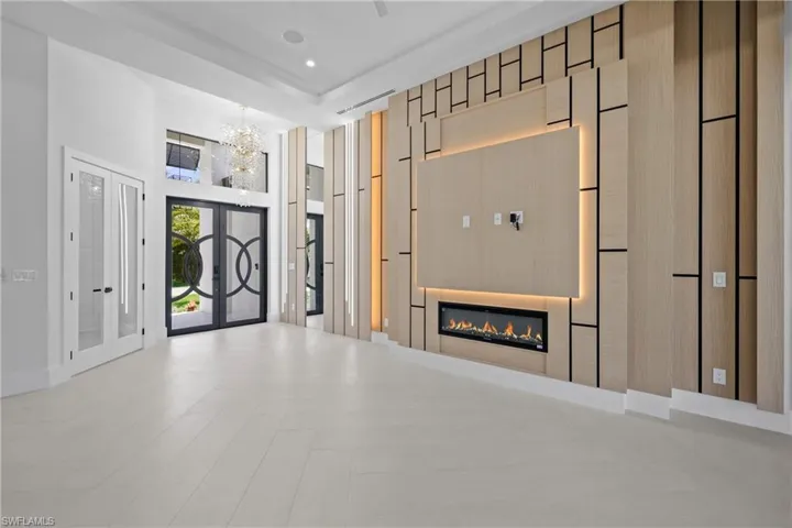 Unfurnished living room with french doors, a glass covered fireplace, a chandelier, and a towering ceiling
