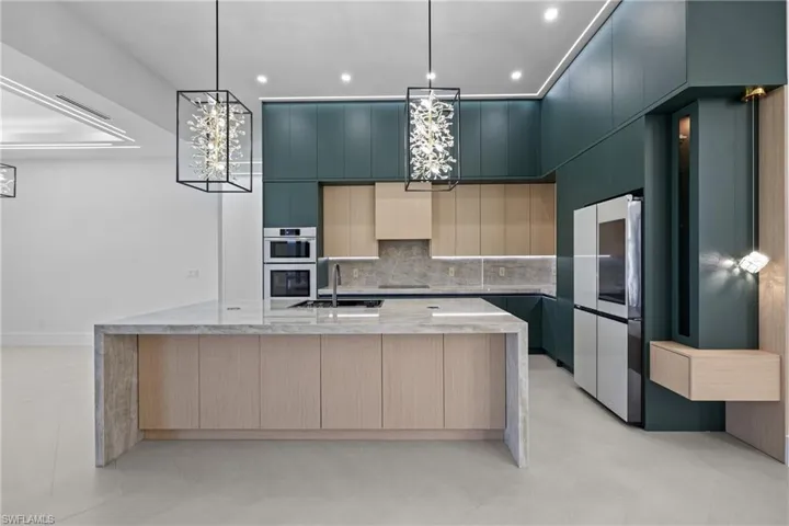 Kitchen featuring smart refrigerator, modern cabinets, a large island with sink, decorative backsplash, and light stone countertops