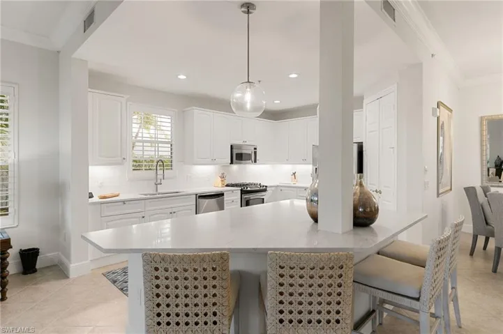 Kitchen featuring crown molding, white cabinets, a kitchen breakfast bar, pendant lighting, and a center island