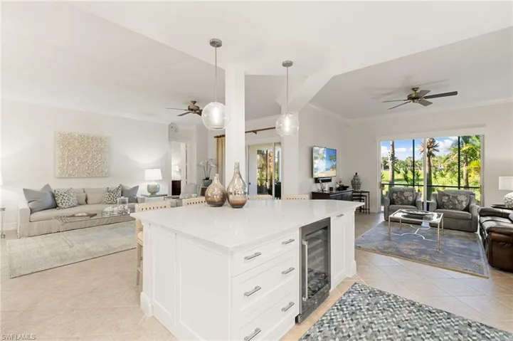 Kitchen featuring open floor plan, crown molding, ceiling fan, light stone countertops, and white cabinets