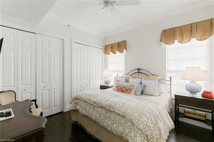 Bedroom featuring multiple closets, dark wood-type flooring, crown molding, and ceiling fan