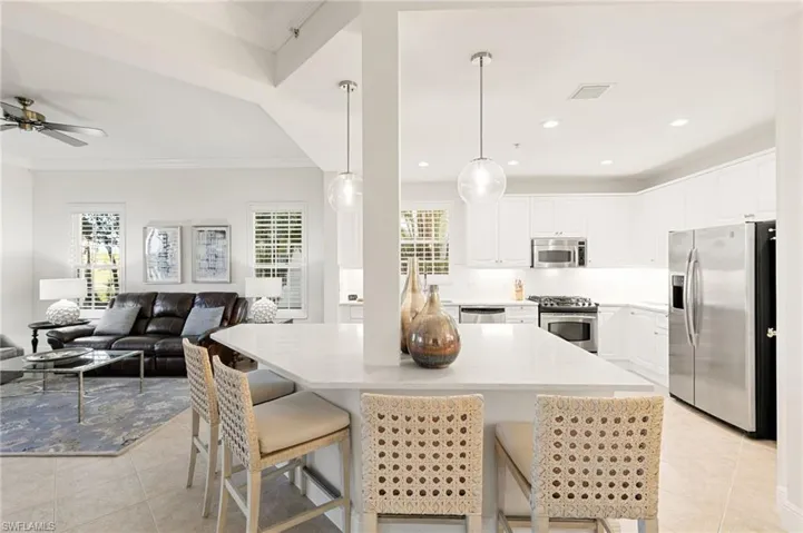 Kitchen with appliances with stainless steel finishes, a kitchen breakfast bar, hanging light fixtures, white cabinets, and light tile patterned floors