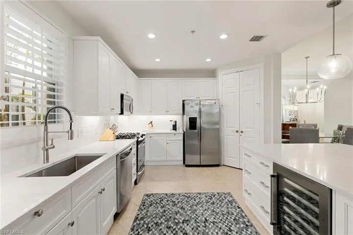 Kitchen with decorative light fixtures, appliances with stainless steel finishes, white cabinets, recessed lighting, and beverage cooler
