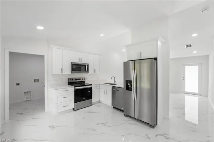 Kitchen with stainless steel appliances, white cabinetry, lofted ceiling, and sink