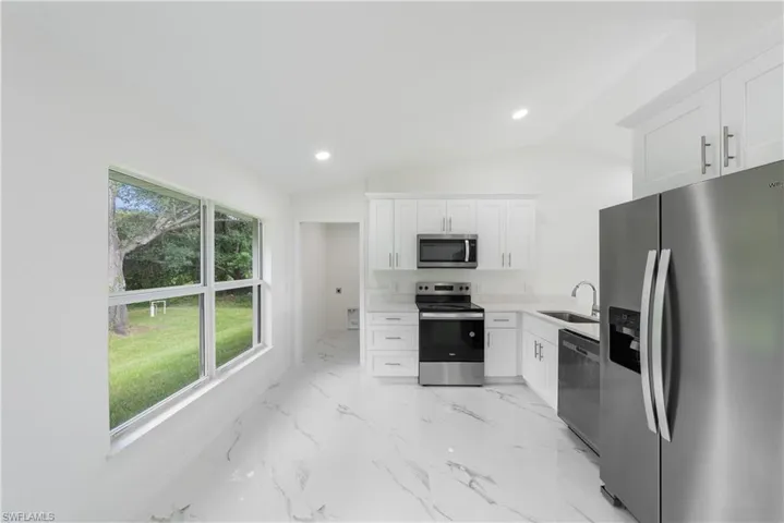 Kitchen with lofted ceiling, appliances with stainless steel finishes, sink, and white cabinets