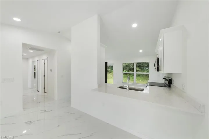 Kitchen with sink, range, light stone countertops, white cabinets, and kitchen peninsula