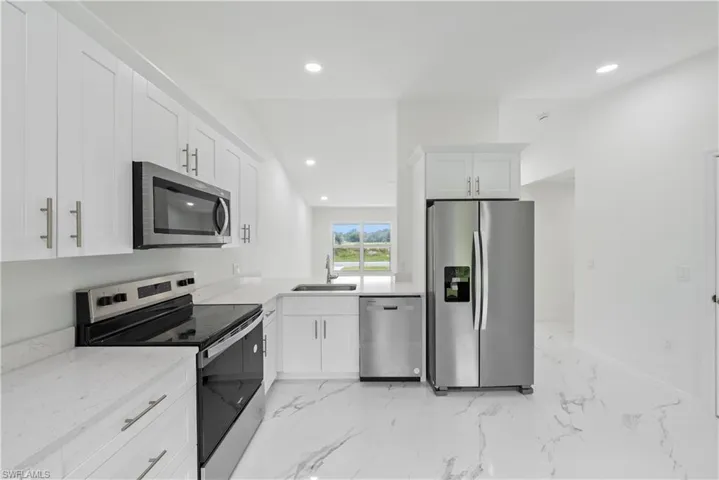 Kitchen with light stone counters, stainless steel appliances, sink, and white cabinets