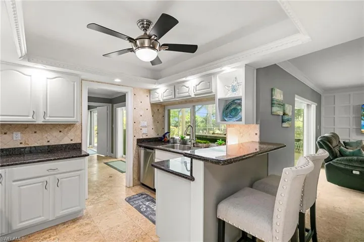 Kitchen featuring stainless steel dishwasher, ornamental molding, a breakfast bar area, decorative backsplash, and white cabinets