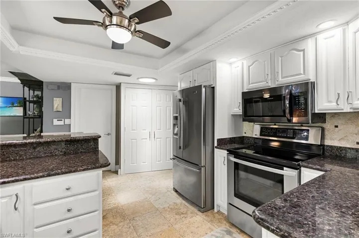 Kitchen with stainless steel appliances, white cabinetry, dark stone counters, and a ceiling fan