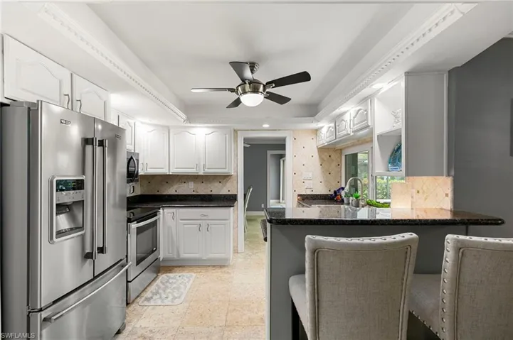 Kitchen with appliances with stainless steel finishes, a peninsula, white cabinets, decorative backsplash, and a ceiling fan
