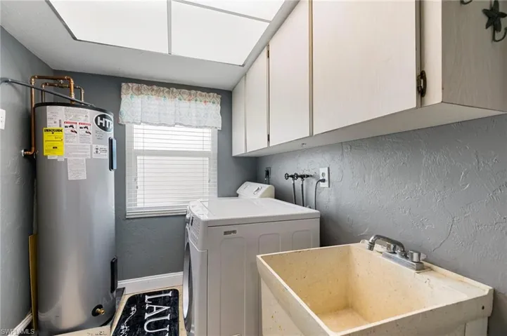 Laundry area with washer / dryer, water heater, cabinet space, and a textured wall