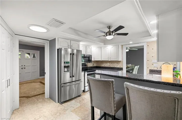 Kitchen featuring appliances with stainless steel finishes, a raised ceiling, ceiling fan, white cabinetry, and recessed lighting