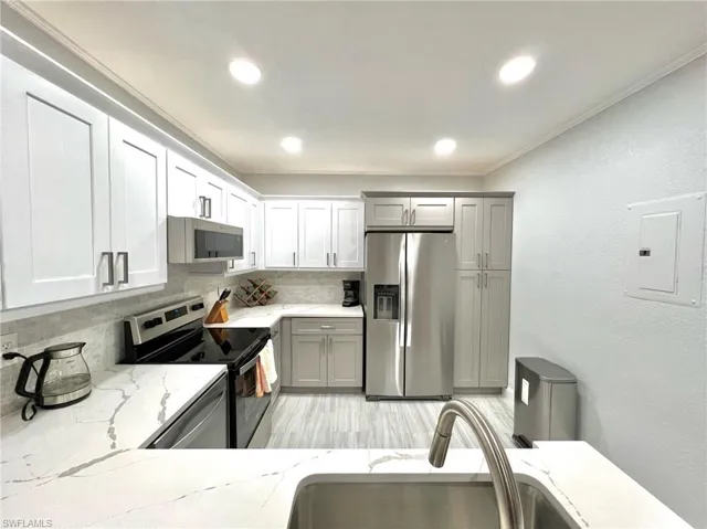Kitchen with electric panel, a sink, backsplash, stainless steel appliances, and light stone countertops