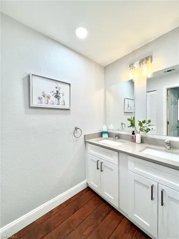 Full bathroom with double vanity, wood finished floors, baseboards, and a sink