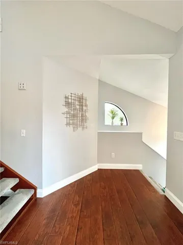 Entrance area top of  stairway, windows to let in light, wood-type flooring, baseboards, and vaulted ceiling