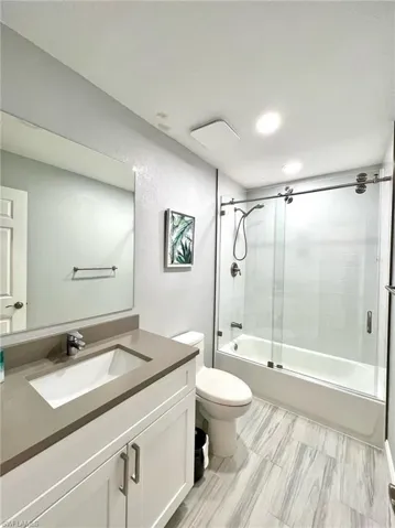 Full guest bathroom featuring vanity, toilet, and enclosed tub / shower combo
