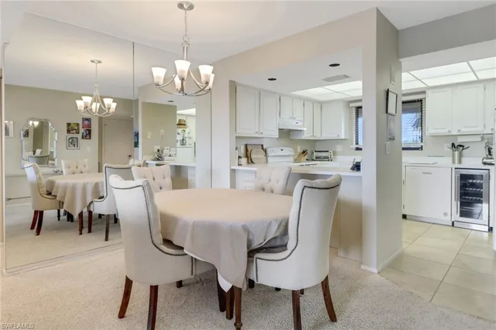Dining area featuring light colored carpet, wine cooler, and a notable chandelier