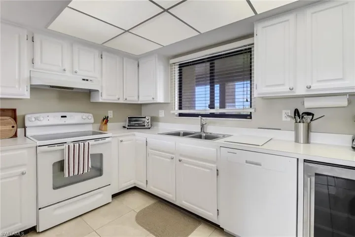 Kitchen featuring white cabinetry, sink, light tile patterned floors, white appliances, and beverage cooler