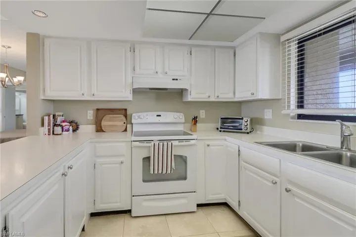 Kitchen with a notable chandelier, light tile patterned floors, sink, white cabinetry, and white range with electric stovetop