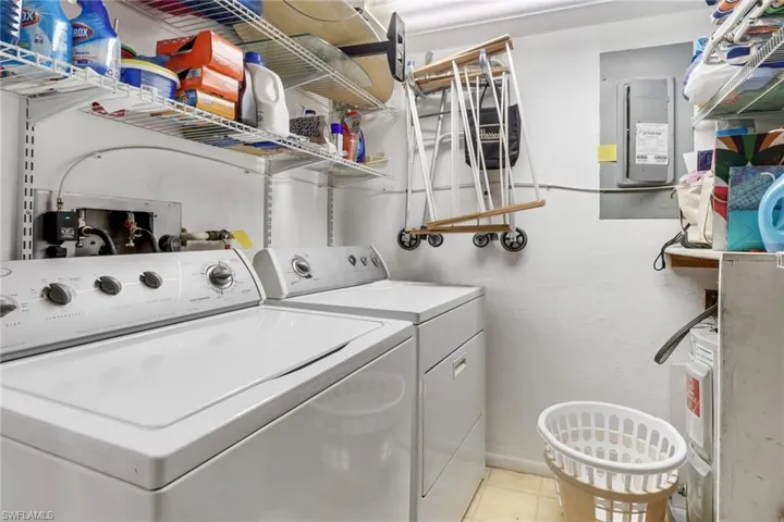 Clothes washing area with washing machine and clothes dryer, light tile patterned floors, and electric panel