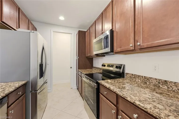 Kitchen featuring appliances with stainless steel finishes, light stone countertops, recessed lighting, brown cabinetry, and light tile patterned flooring