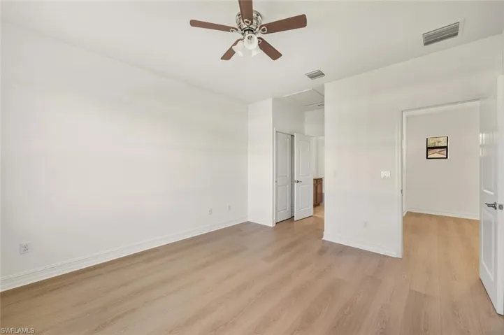 Unfurnished bedroom featuring light wood-style flooring, attic access, and a ceiling fan