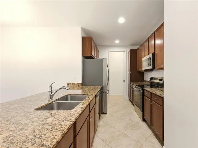 Kitchen featuring appliances with stainless steel finishes, dark stone countertops, brown cabinetry, light tile patterned flooring, and recessed lighting