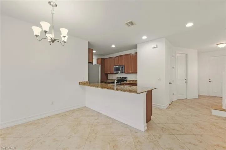 Kitchen with brown cabinets, decorative light fixtures, a peninsula, appliances with stainless steel finishes, and dark stone counters