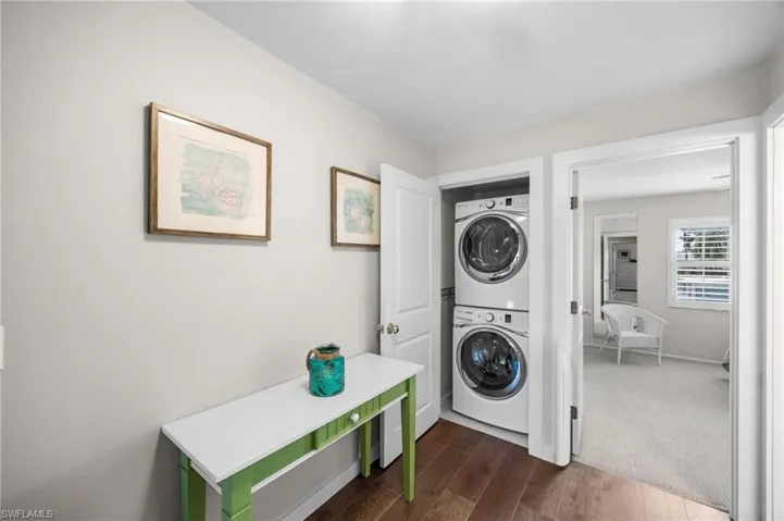 Washroom with dark wood-type flooring, stacked washer / dryer, and dark colored carpet
