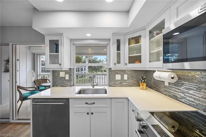 Kitchen featuring white cabinets, appliances with stainless steel finishes, light stone countertops, glass insert cabinets, and tasteful backsplash