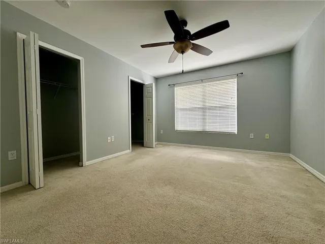 Unfurnished bedroom featuring light carpet, a closet, ceiling fan, and a walk in closet