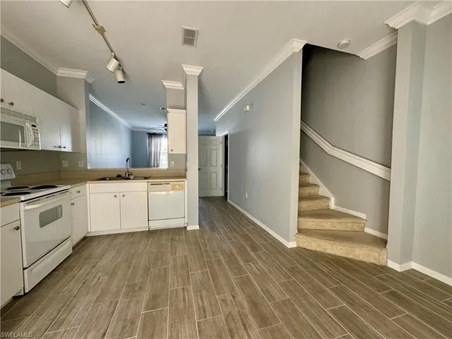 Kitchen with white appliances, sink, dark wood-type flooring, and white cabinets