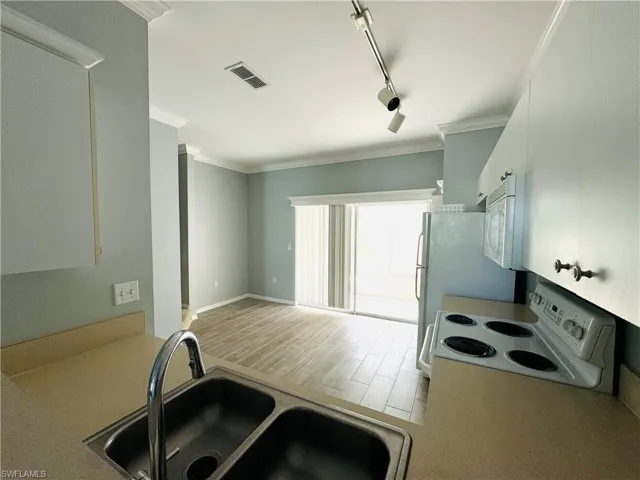 Kitchen with white cabinets, sink, white appliances, rail lighting, and light hardwood / wood-style floors