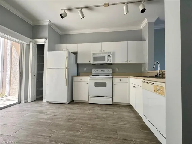 Kitchen with rail lighting, white cabinets, white appliances, crown molding, and sink