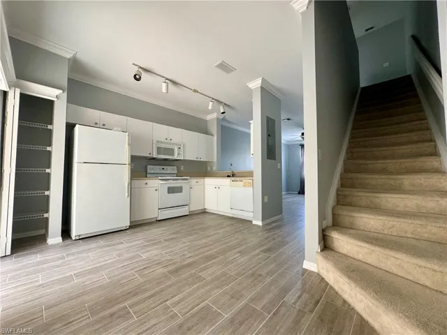 Kitchen with ornamental molding, white appliances, track lighting, and white cabinetry