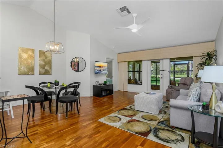 Living area with lofted ceiling, wood finished floors, a ceiling fan, a chandelier, and baseboards