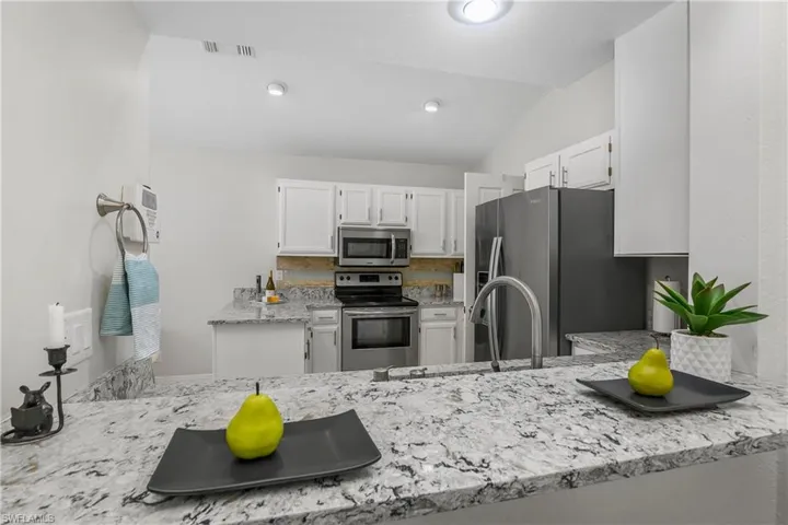 Kitchen featuring stainless steel appliances, vaulted ceiling, white cabinets, light stone countertops, and a peninsula