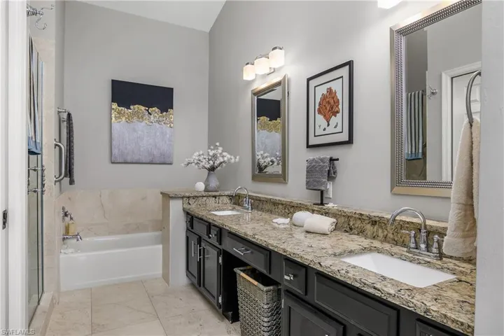Bathroom featuring a bath, double vanity, marble look tile flooring, and a shower stall