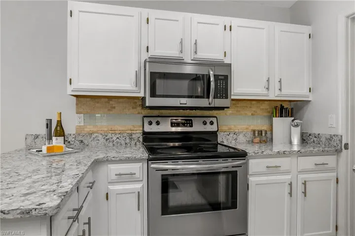 Kitchen featuring stainless steel appliances, white cabinetry, and backsplash