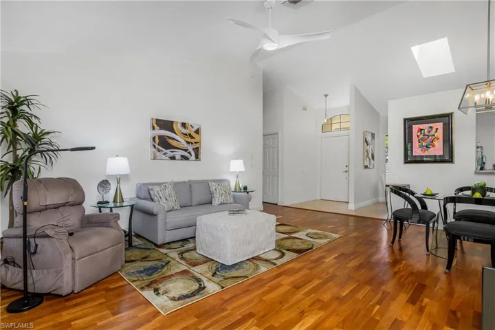 Living area with a skylight, wood finished floors, high vaulted ceiling, ceiling fan, and baseboards