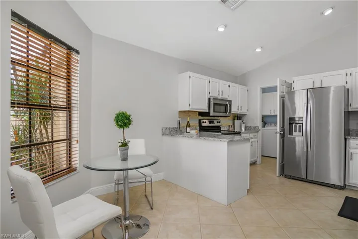 Kitchen with appliances with stainless steel finishes, lofted ceiling, white cabinetry, a peninsula, and light stone countertops