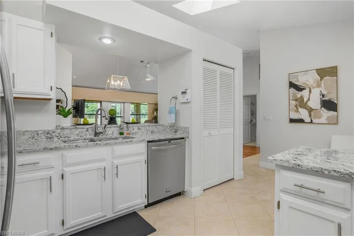 Kitchen with stainless steel dishwasher, a sink, white cabinets, a skylight, and light tile patterned floors