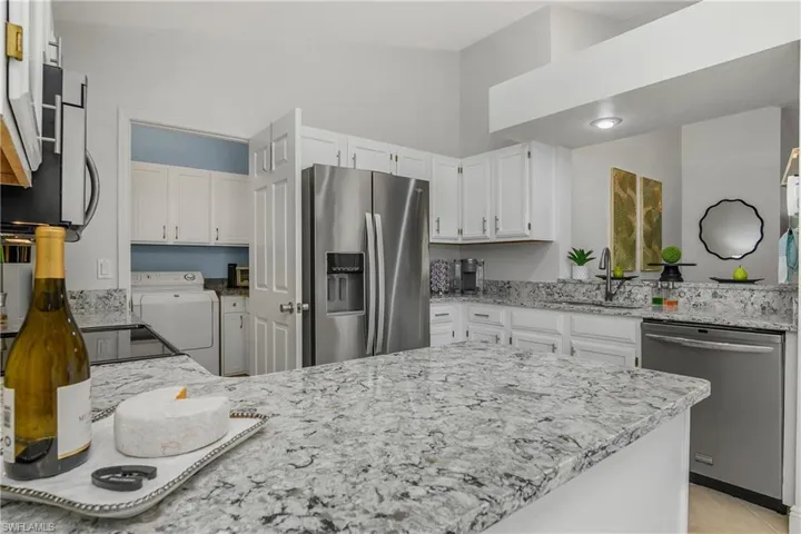 Kitchen with appliances with stainless steel finishes, a sink, light stone countertops, a peninsula, and white cabinets