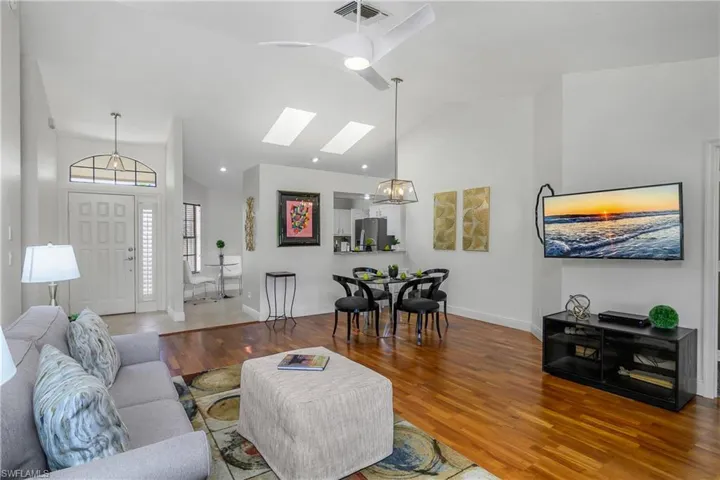 Living area featuring lofted ceiling, wood finished floors, a skylight, baseboards, and a chandelier